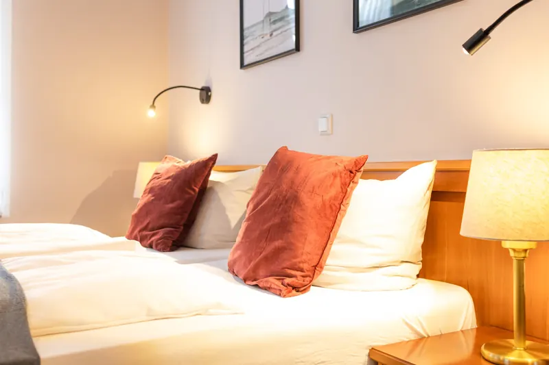 Detail im Doppelzimmer: Samtkissen, frische Bettwäsche und Leseleuchte