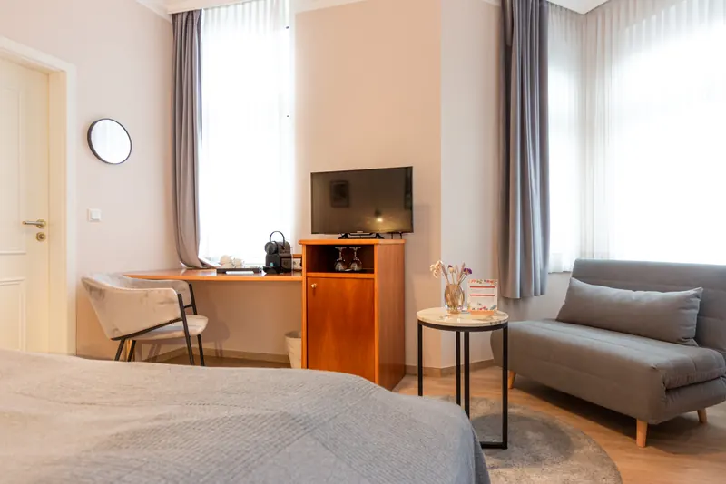 Doppelzimmer mit Schreibtisch, Fernseher, Kaffeemaschine und Schlafsofa am Fenster