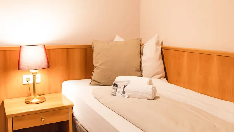 Einzelzimmer mit Holzvertäfelung, Nachttischlampe und frisch bezogenem Bett mit Handtüchern